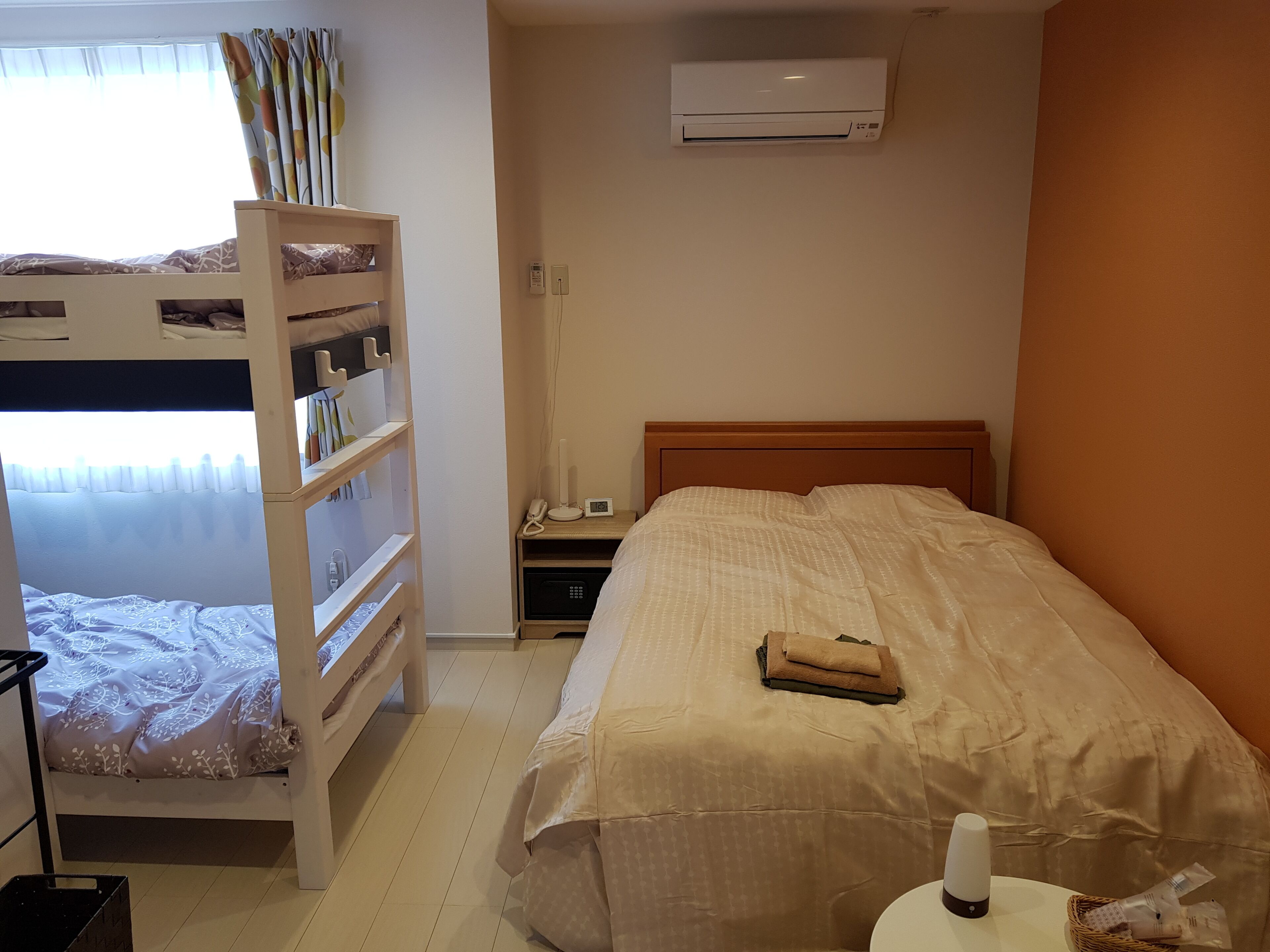 Une chambre avec un lit superposé, une table de chevet avec un téléphone et une lampe, un climatiseur et un petit panier placé à côté du lit.