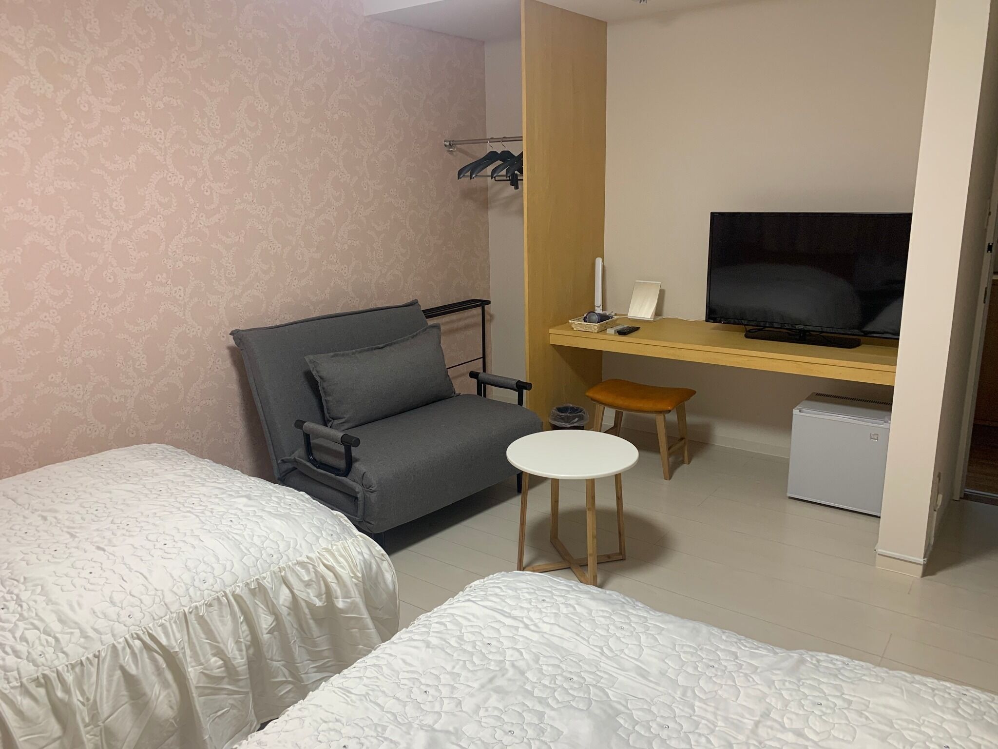 A hotel room with two beds, a desk with a TV, a small table, and a chair.