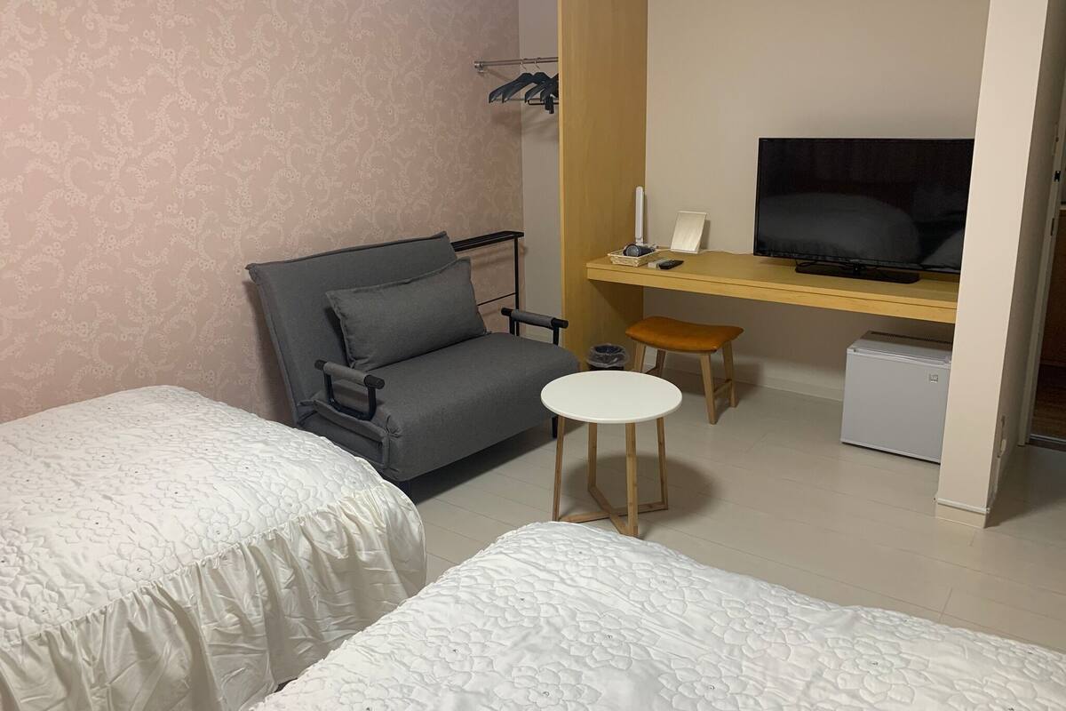 Quarto de hotel com cama, sofá, mesinha, televisão e secretária com computador.
