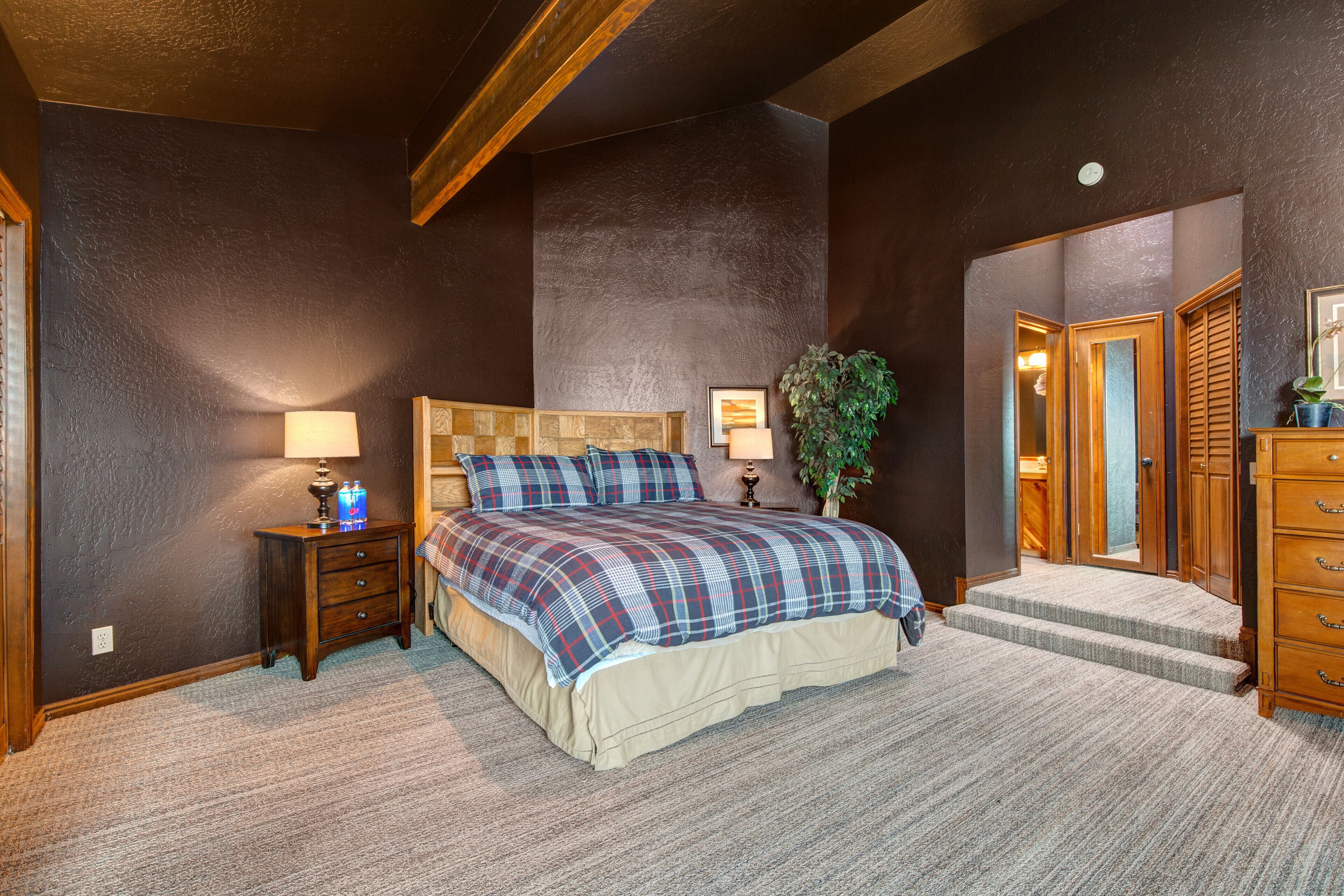 A bedroom with a large bed, a nightstand, a dresser, and a door leading to another room.