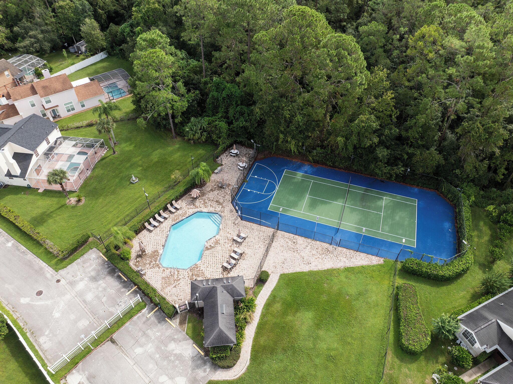 An aerial view of a residential property with a tennis court, swimming pool, and a house with a covered patio.