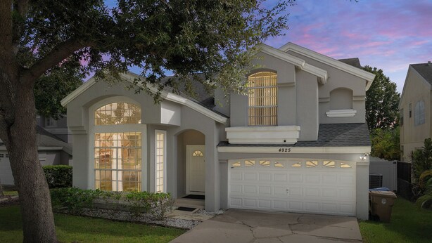 A two-story house with a garage, large windows, and a tree in the front yard. - Luxury Villa with private  pool and heated Jacuzzi (Kissimmee)
