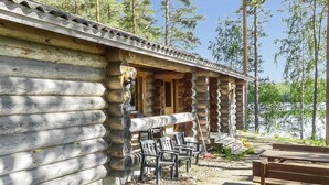 A log cabin with a porch, outdoor seating, and a view of a forested area.