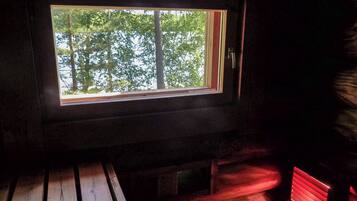 Ein Zimmer mit Fenster, das auf einen Wald blickt, eine Holzbank und eine rot beleuchtete Wand.