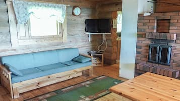 Un accogliente interno di una baita con un divano in legno, un televisore fissato alla parete, un camino in mattoni e un tavolo da pranzo in legno.