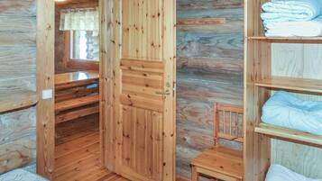 A wooden cabin interior with a bed, a chair, and a shelf with folded blankets.