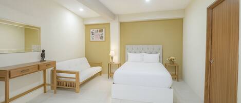 A bedroom with a bed, a desk, a chair, a bedside table, a lamp, and a wooden wardrobe.