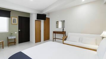 Un dormitorio con cama, un sofá blanco, televisión, espejo y una pequeña mesa con lámpara.