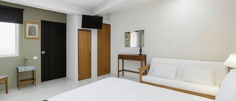 A bedroom with a bed, a white sofa, a TV, a mirror, and a small table with a lamp.