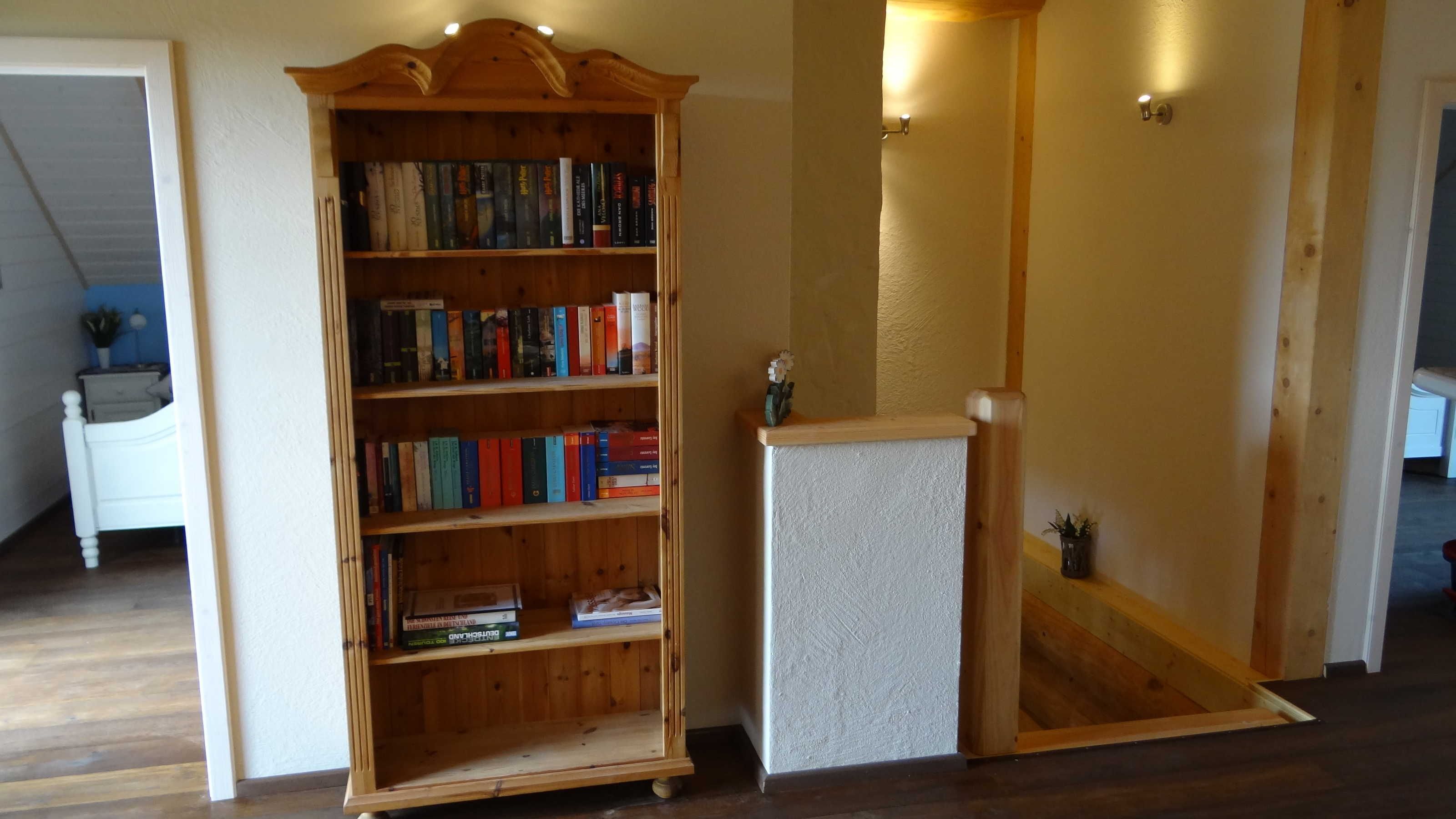 A wooden bookshelf filled with books, a small white table with a vase, and a wooden bench.