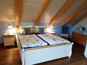 A bedroom with a wooden ceiling, two beds with floral bedding, bedside lamps, and a dresser.