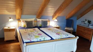 Ein Schlafzimmer mit Holzbalkendecke, zwei Betten mit floralem Bettzeug, Nachttischlampen und einer Kommode.