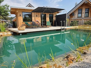 Una cabaña de madera con piscina, mobiliario exterior y un patio cubierto.