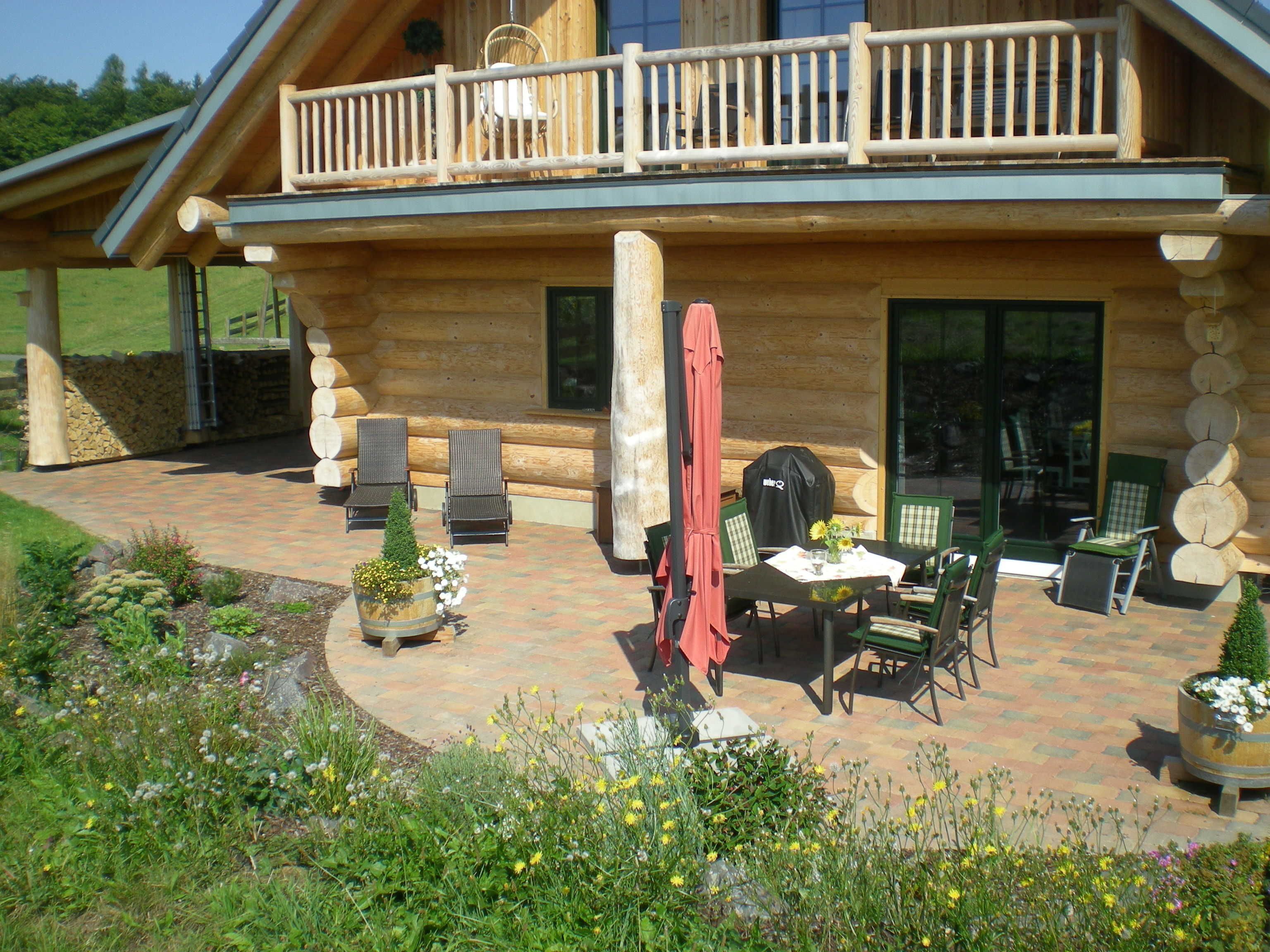 A log cabin with a balcony, outdoor seating area, and a garden.