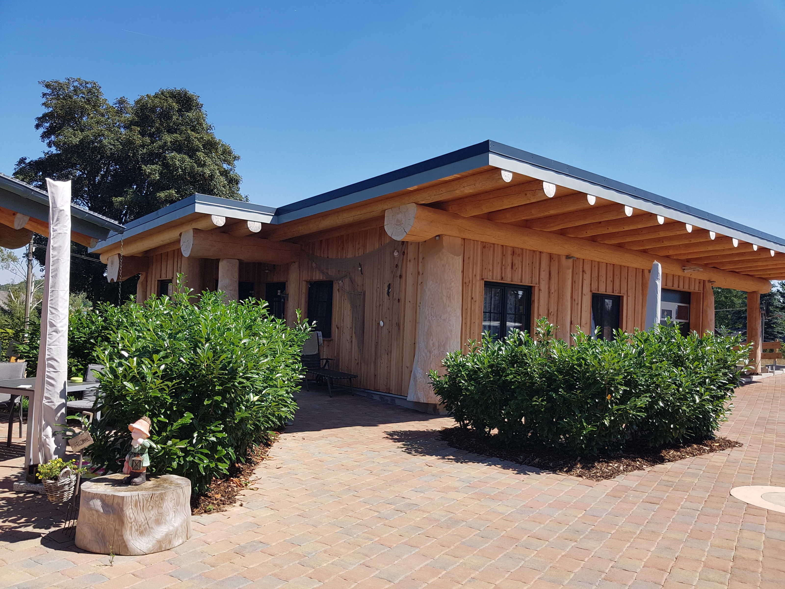 A wooden building with a covered patio area, a welcome sign, and a small garden with a welcome figurine.