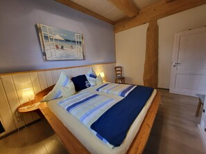 A bed with a striped bedspread, a wooden headboard, and a painting of a beach scene above it. - Fischerhütte - Steirer-Hof (Vöhl)