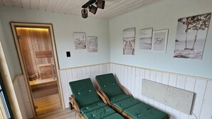 Habitació amb terres de fusta, dos llits verds, una banca de fusta, una porta de fusta i una paret amb quadres emmarcats.