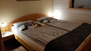 A bedroom with a wooden headboard, two beds with checkered bedding, a nightstand, a lamp, a painting of a landscape, and a window with curtains. - Hunting lodge - Steirer-Hof (Vöhl)