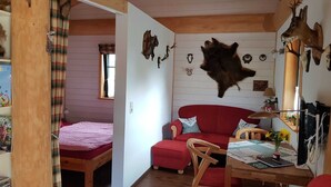 Una habitació acollidora amb sostre de fusta, un sofà vermell, una taula petita amb una làmpada i diverses pells i corns d'animals a les parets.