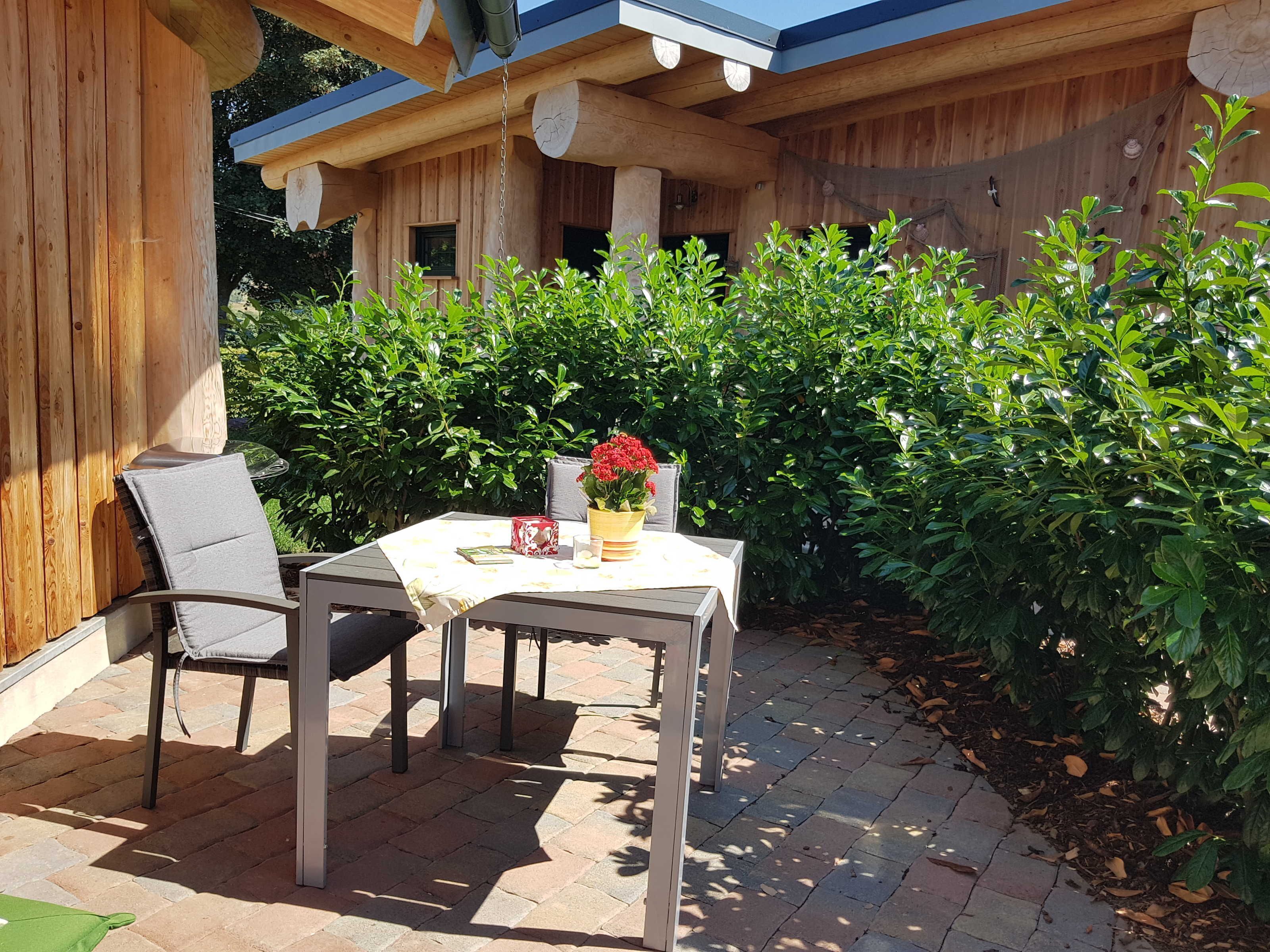 Eine Terrasse im Freien mit Tisch und Stühlen, umgeben von üppiger Vegetation und Holzbauten.