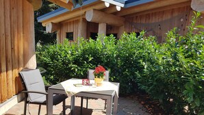 An outdoor patio with a table and chairs, surrounded by lush greenery and wooden structures. - Hunting lodge - Steirer-Hof (Vöhl)
