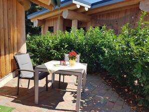 An outdoor patio with a table and chairs, surrounded by lush greenery and wooden structures. - Hunting lodge - Steirer-Hof (Vöhl)