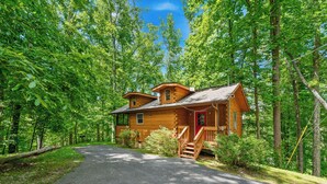 A wooden cabin with a porch and a driveway, surrounded by dense forest. - Secluded Cabin w/ Hot Tub • King Bed • Smoky Mountains (Sevierville)
