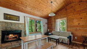 A cozy cabin interior with a stone fireplace, wooden ceiling, and a sofa by a window. - Secluded Cabin w/ Hot Tub • King Bed • Smoky Mountains (Sevierville)