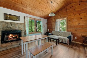 Cozy cabin with a stone fireplace, comfortable seating area, and large windows offering a view of the surrounding trees.