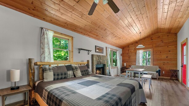 A cozy log cabin bedroom with a large bed, a fireplace, a dining table, and a view of the outdoors. - Secluded Cabin w/ Hot Tub • King Bed • Smoky Mountains (Sevierville)