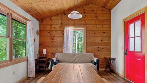 A cozy cabin interior with a wooden dining table, a sofa, and a red door. - Secluded Cabin w/ Hot Tub • King Bed • Smoky Mountains (Sevierville)