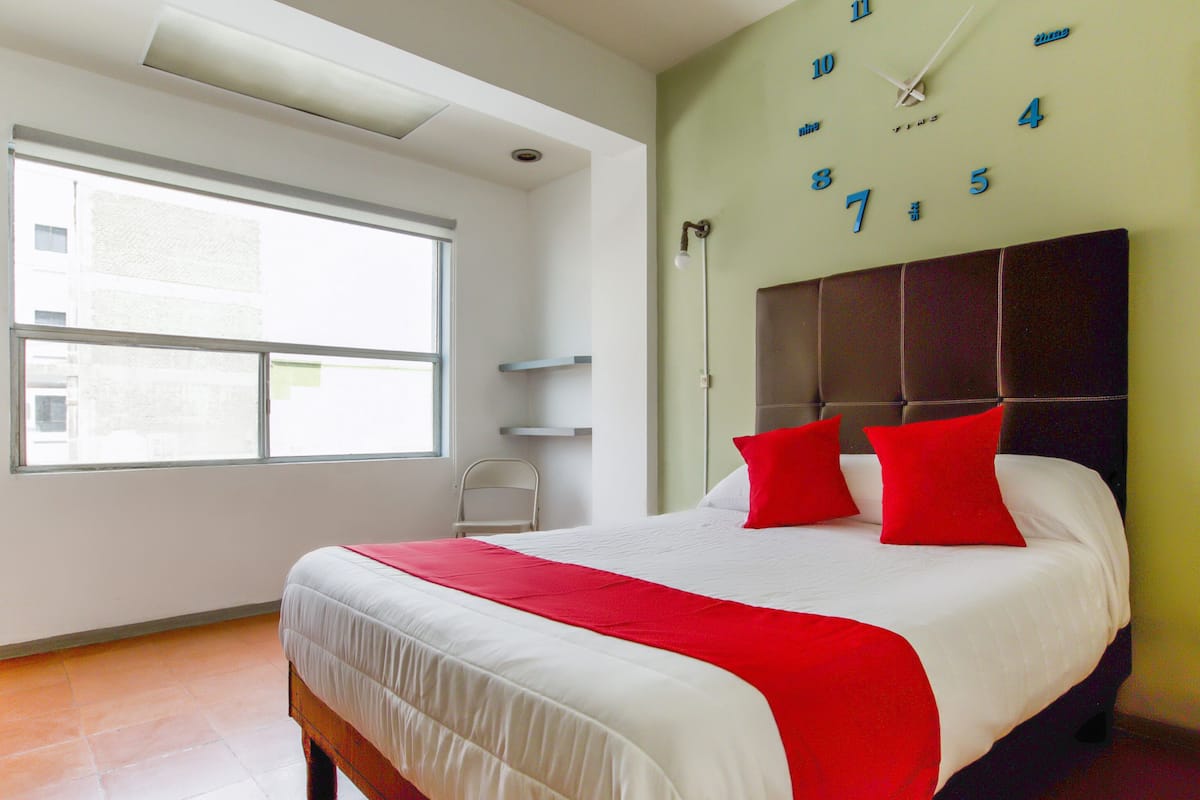 Ein modernes Hotelzimmer mit einem großen Bett, einem Fenster und einer Wanduhr.