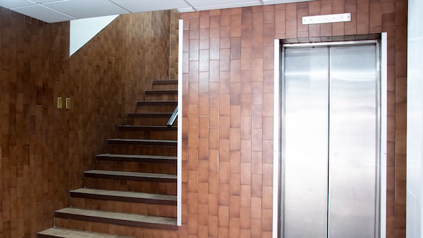 A staircase leading to an elevator in a building with a brown brick wall. - Hotel Allende 104 (Chihuahua)