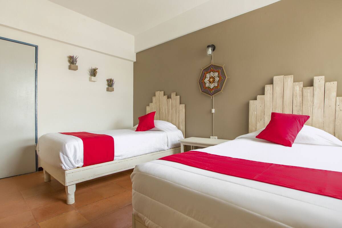 Ein Hotelzimmer mit zwei Betten, jeweils mit weißer Bettwäsche und roten Kissen, einem Holz-Kopfteil und einem dekorativen Wandbild.