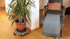 Une pièce avec un escalier en bois, une plante en pot, une chaise noire avec un coussin et une couverture grise.