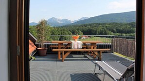 Un balcon avec une table et des chaises en bois, un pot de fleurs et une vue sur les montagnes.