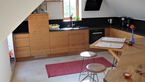 Une cuisine compacte avec des meubles en bois, un plan de travail noir, une fenêtre et un petit coin repas équipé de tabourets.