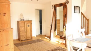 Une pièce comprenant un meuble en bois, un miroir, une table avec des chaises et une porte donnant sur une autre pièce.