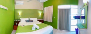 A hotel room with a bed, a nightstand, a potted plant, a window with curtains, and a bathroom with a mirror and sink. - Hotel Casa Mia (Puerto Escondido)
