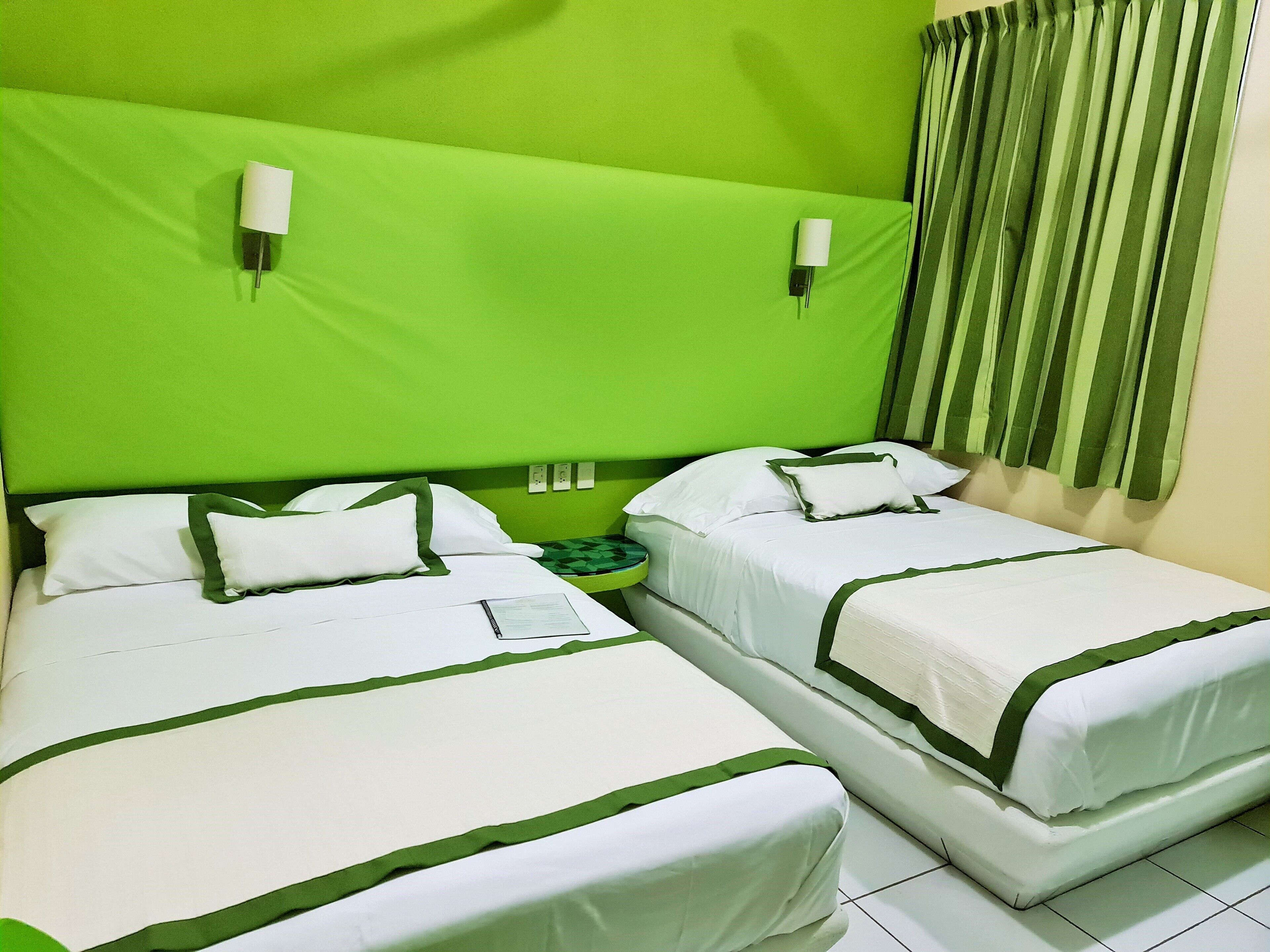 Une chambre d’hôtel avec deux lits, chacun doté de draps blancs et d’une bordure verte. Deux lampes murales sont fixées au-dessus de la tête de lit.