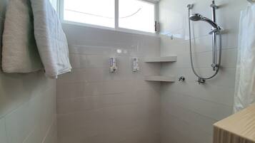 A modern bathroom with white tiles, a shower with a handheld showerhead, and a window providing natural light.
