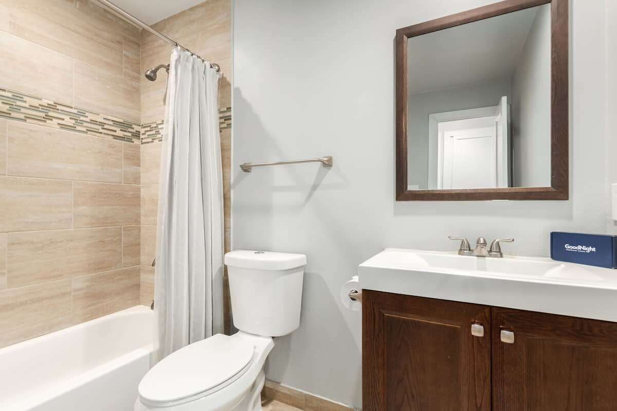 Une salle de bain avec une baignoire, des toilettes, un rideau de douche et un miroir au-dessus du lavabo.