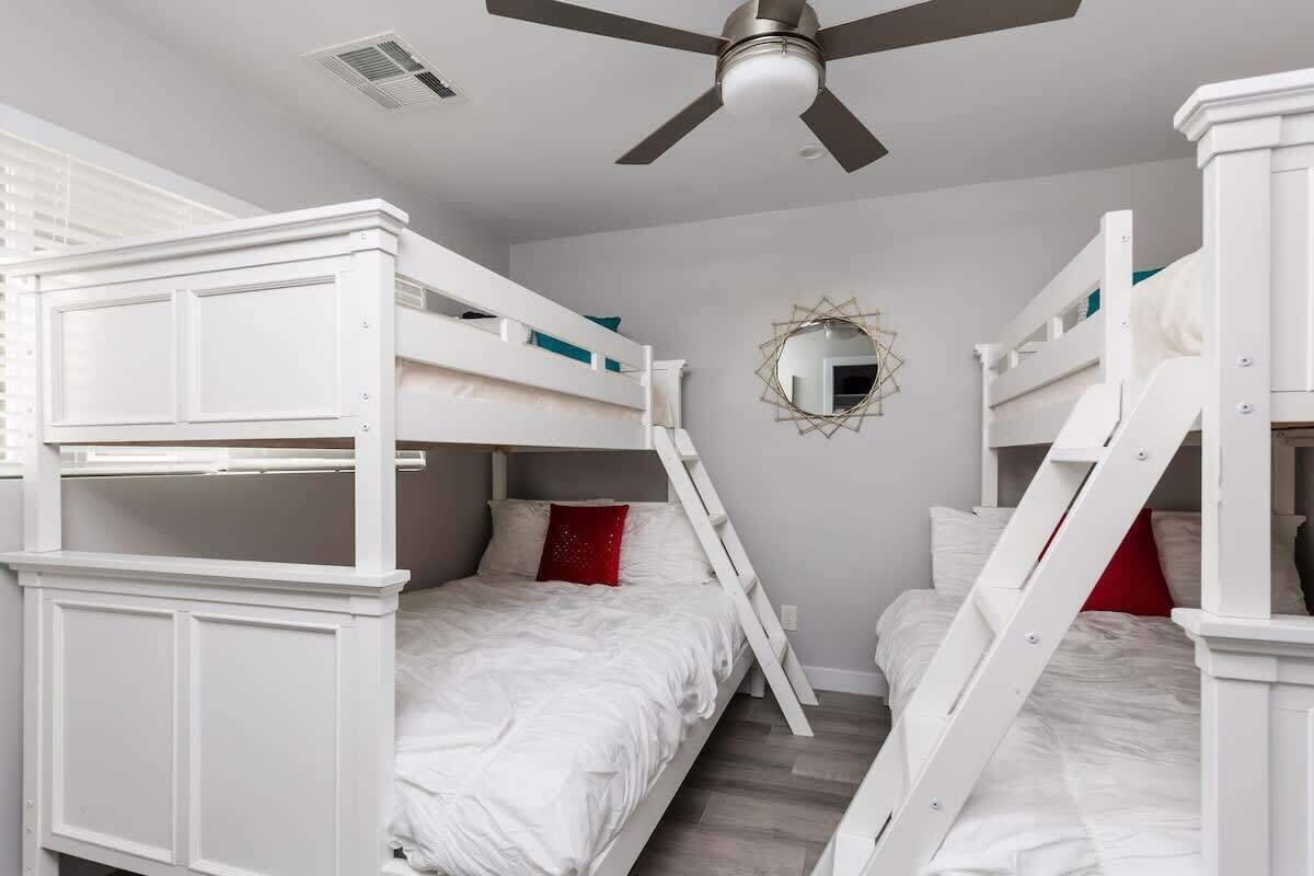 A bunk bed room with a ceiling fan, a decorative mirror, and a ladder.