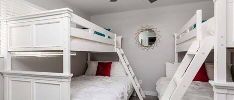 A bunk bed room with a ceiling fan, a decorative mirror, and a ladder.