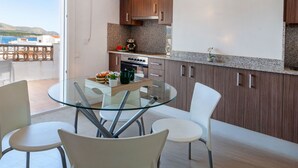 Une cuisine moderne avec une table et des chaises en verre, des meubles en bois et une vue sur la mer.