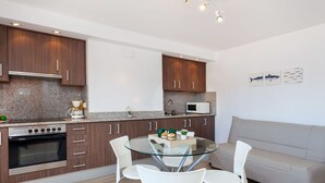 Une cuisine moderne dotée de plans de travail en granit, d’un four encastré et d’un four à micro-ondes. On y trouve une table à manger en verre, accompagnée de quatre chaises.