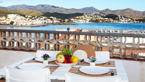 Une table dressée pour deux personnes, avec vue sur une ville côtière et des montagnes en arrière-plan.