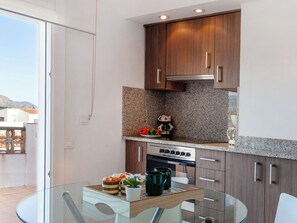 A modern kitchen with wooden cabinets, a granite countertop, and a glass dining table. - Blue Ocean by Interhome (Llançà)