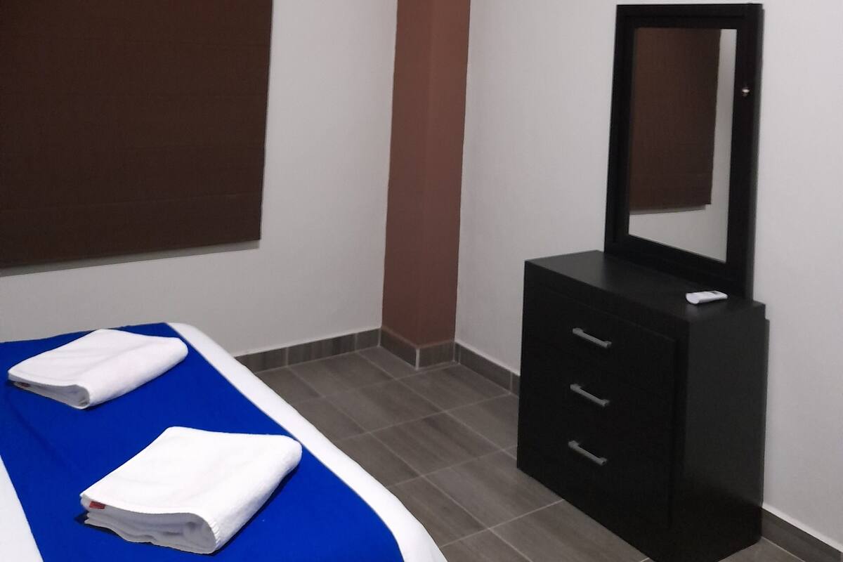 Un dormitorio con cama, cómoda, espejo, ventilador de techo y aire acondicionado.
