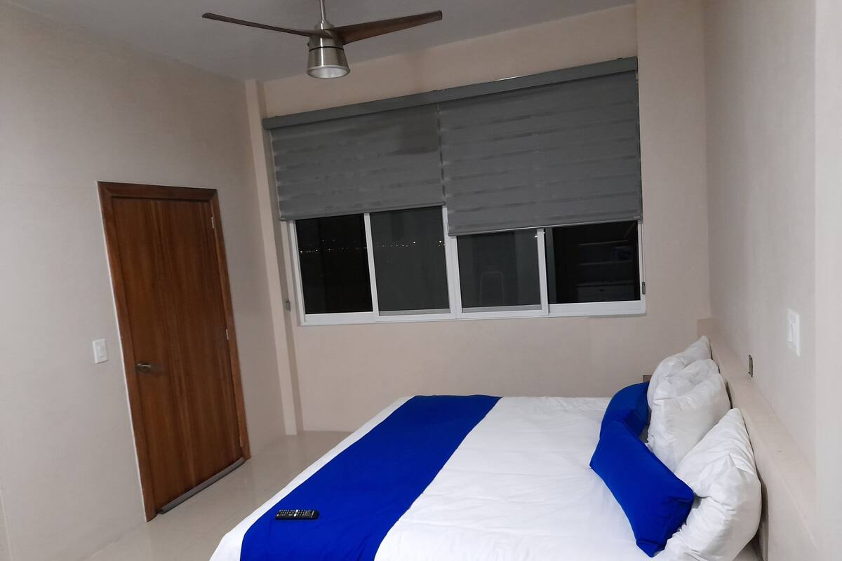 Un dormitorio con cama, ventana con persianas, ventilador de techo y puerta.